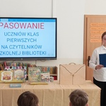 Tablica z napisem Pasowanie na czytelników i uczennica prowadząca uroczystość.