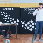 przedstawienie uczeń siedzi przy szkolnej ławce, drugi mówi do mikrofonu