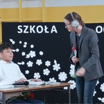 scena z przedstawienia-siedzący za ławką dwaj uczniowie i uczennica grająca nauczycielkę