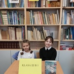drużyna 1 z klasy 3b -dwie dziewczynki, siedzące przy stoliku na tle regałów z książkami