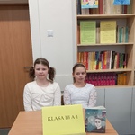 drużyna 1 z klasy 3a -dwie dziewczynki, siedzące przy stoliku na tle regałów z książkami