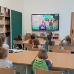 siedzi siedzą przy stolikach i oglądają film z panią Celiną Zubrycką