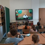 Dzieci patrzą w telewizor. Na ekranie pani Elżbieta Janikowska z otwartą książką 