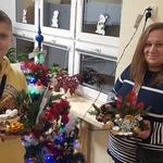 chłopiec trzyma stroik, obok jego mama trzymająca stroik, w tle ubrana choinka