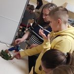 mama z synem stoją przy stoliku i wykonują stroik. w oddali pracują inni rodzice, widać głowy dzieci