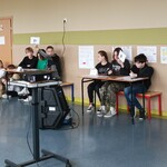 trzy zespoły podnoszą kartki z odpowiedzią, w tle publiczność
