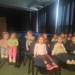 dzieci siedzą w sali teatralnej na krzesłach