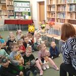 dzieci siedzą na dywanie, pani bibliotekarka pokazuje kartkę