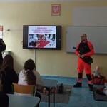 Strażnik miejski i ratownik medyczny w klasie na zajęciach z młodzieżą. Na ekranie napis: Szkolenie z zakresu udzielania pierwszej pomocy