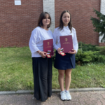 Nauczycielka i uczennica z medalami Diligentiae przed szkołą
