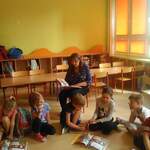 Pani Jolanta czyta dzieciom książkę, dzieci siedzą na podłodze przy otwartych książkach