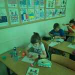 uczniowie siedzą w ławkach i wykonują prace plastyczne