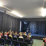 W sali teatralnej pani policjantka siedzi na krześle na scenie- dzieci na widowni
