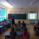 Strażnik miejski w sali lekcyjnej z uczniami, którzy siedzą w ławkach