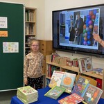Pani bibliotekarka pokazuje dzieciom na ekranie zdjęcie z wręczania nagrody ich koleżance z klasy.