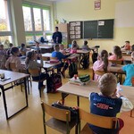 Policjantka omawia zasady bezpiecznego poruszania się po drodze a dzieci uważnie jej słuchają