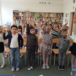 Uczniowie klasy pierwszej z uniesionymi w górze dwoma palcami prawej ręki powtarzają tekst pasowania na czytelnika biblioteki szkolnej