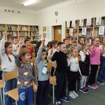 Uczniowie klasy pierwszej z uniesionymi w górze dwoma palcami prawej ręki powtarzają tekst pasowania na czytelnika biblioteki szkolnej