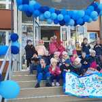 1.Przedszkolaki prezentują plakat przy wejściu do przedszkola. W tle girlanda z niebieskich balonów