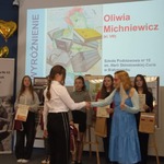 Uczennica klasy 8B podczas rozdania nagród w ramach Wojewódzkiego Konkursu Plastycznego CZYTANIE JEST THE BEST! W tle wyróżniona praca.